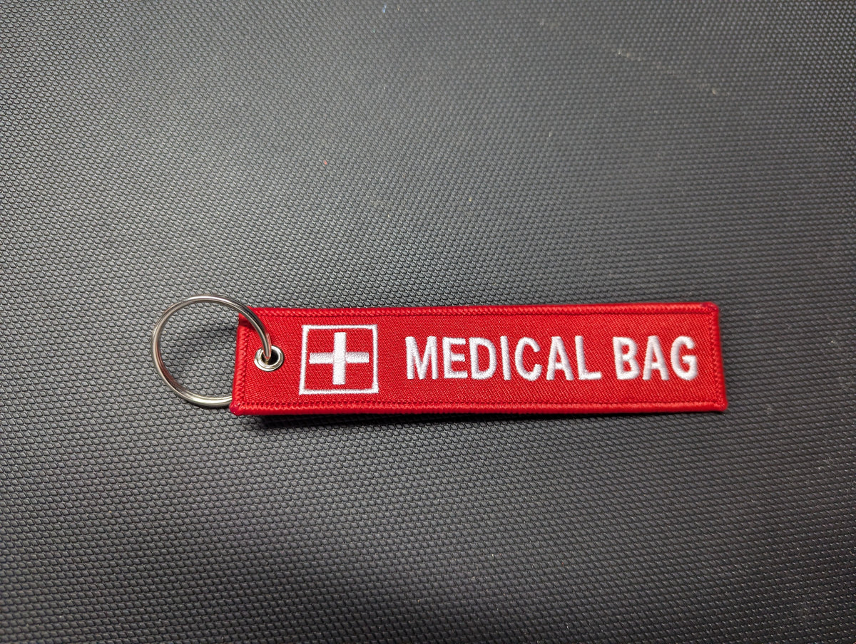 Red Medical Bag fabric keychain, oriented upright, embroidered white lettering and medical cross